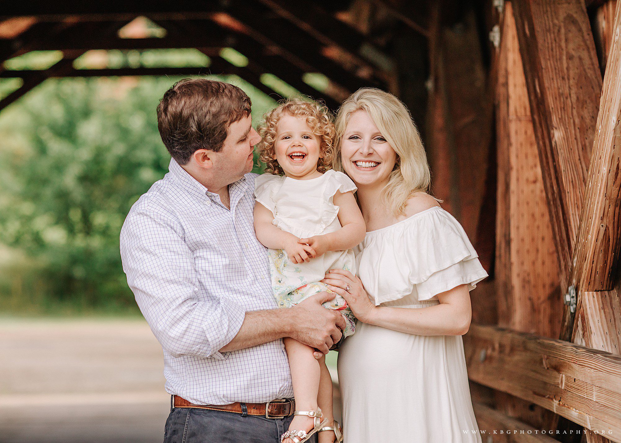 Marietta family photographer - husband, daughter, and mother posing under a covered bridge